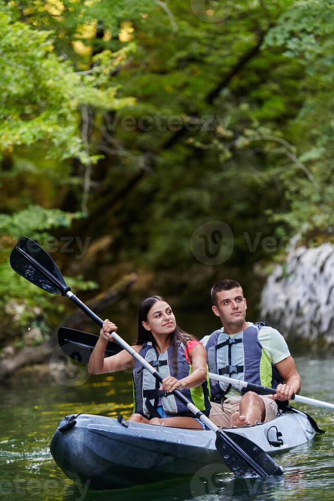 A young couple enjoying an idyllic kayak ride in the middle of a beautiful river surrounded by forest greenery photo