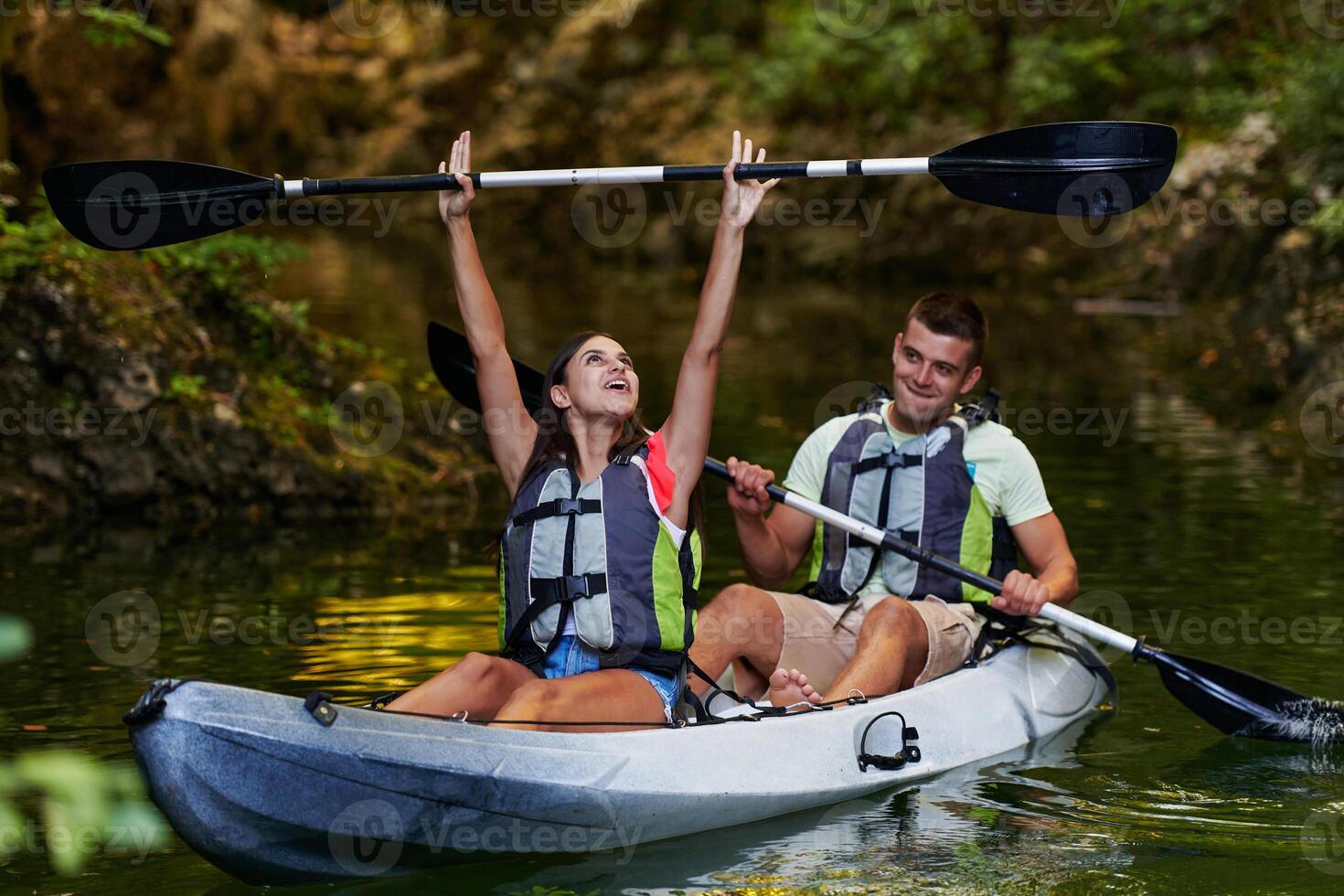 A young couple enjoying an idyllic kayak ride in the middle of a beautiful river surrounded by forest greenery photo