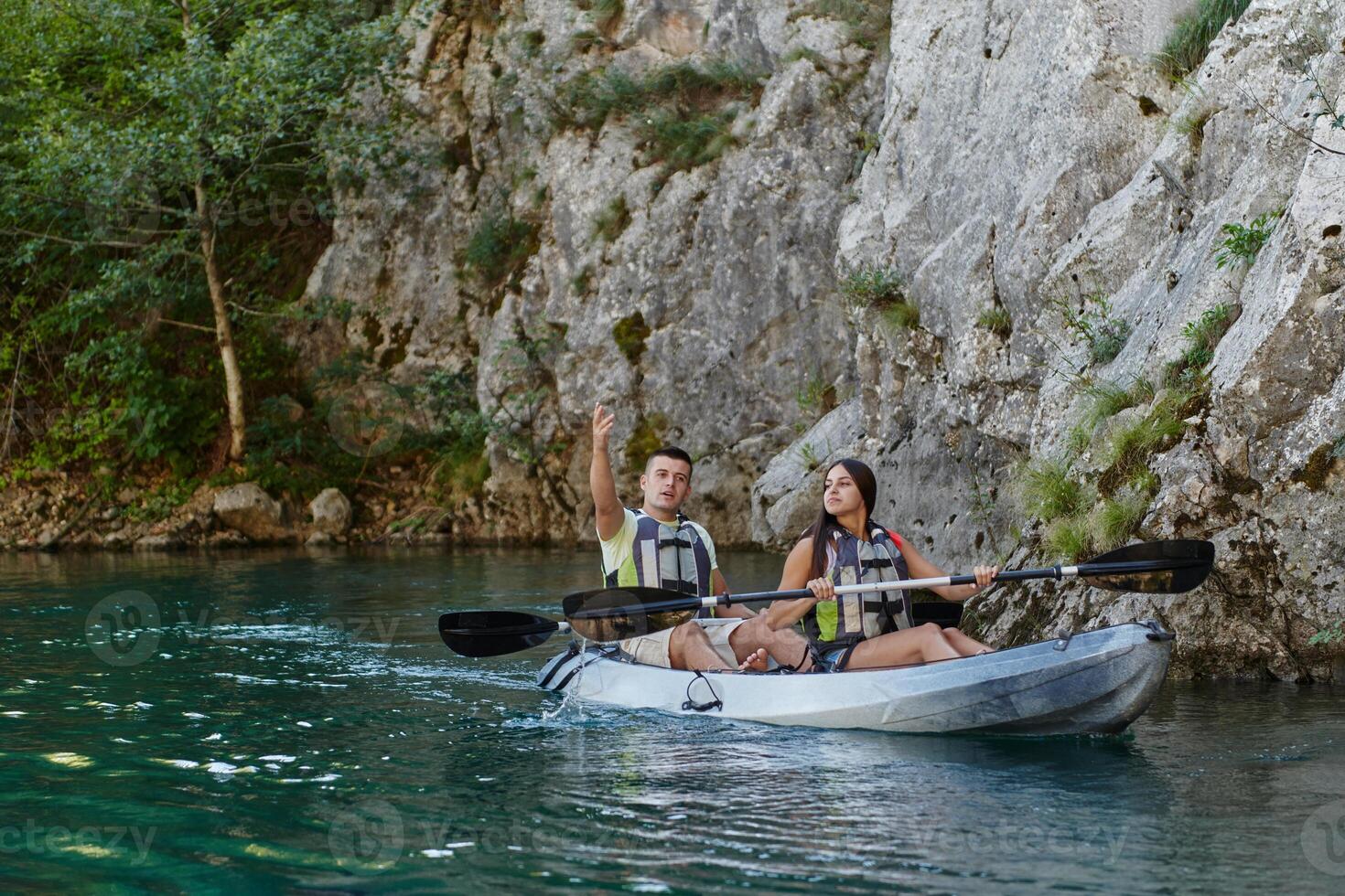 A young couple enjoying an idyllic kayak ride in the middle of a beautiful river surrounded by forest greenery photo