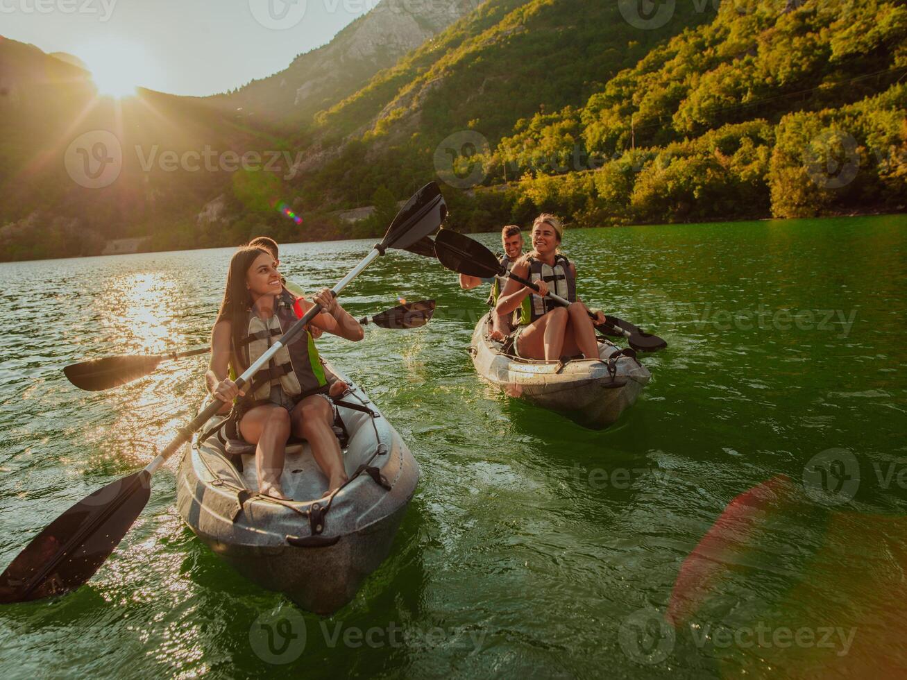 A group of friends enjoying fun and kayaking exploring the calm river, surrounding forest and large natural river canyons during an idyllic sunset. photo