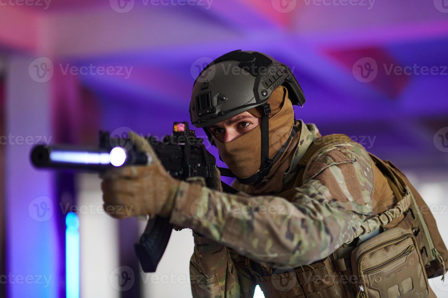 A professional soldier undertakes a perilous mission in an abandoned building illuminated by neon blue and purple lights photo