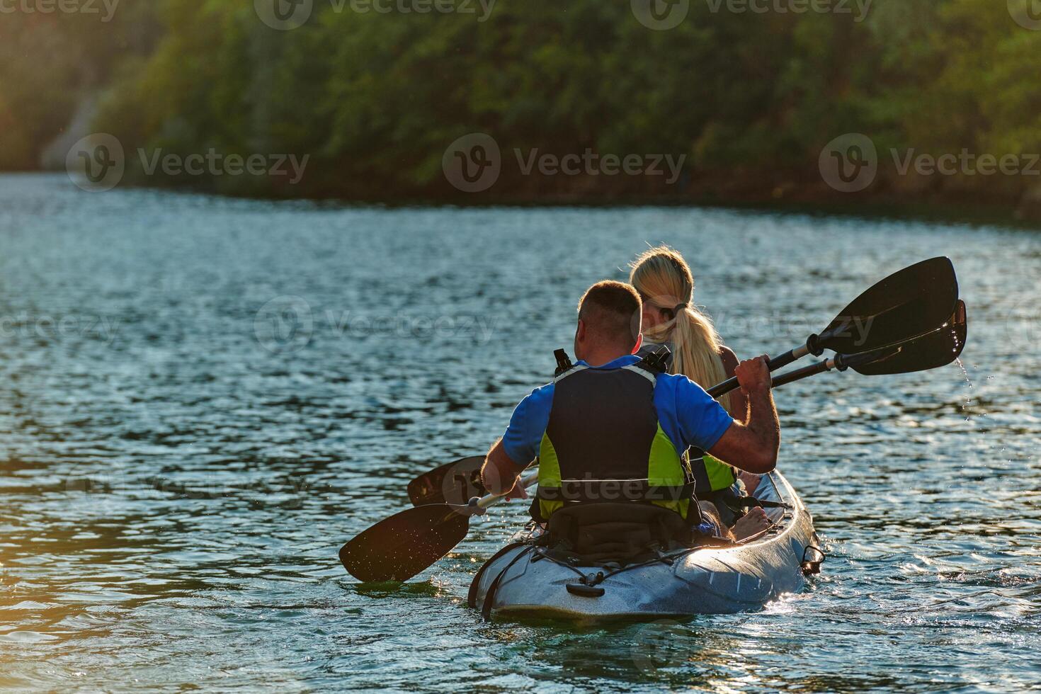 A young couple enjoying an idyllic kayak ride in the middle of a beautiful river surrounded by forest greenery in sunset time photo