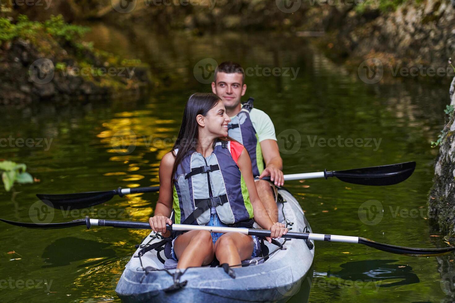 A young couple enjoying an idyllic kayak ride in the middle of a beautiful river surrounded by forest greenery photo