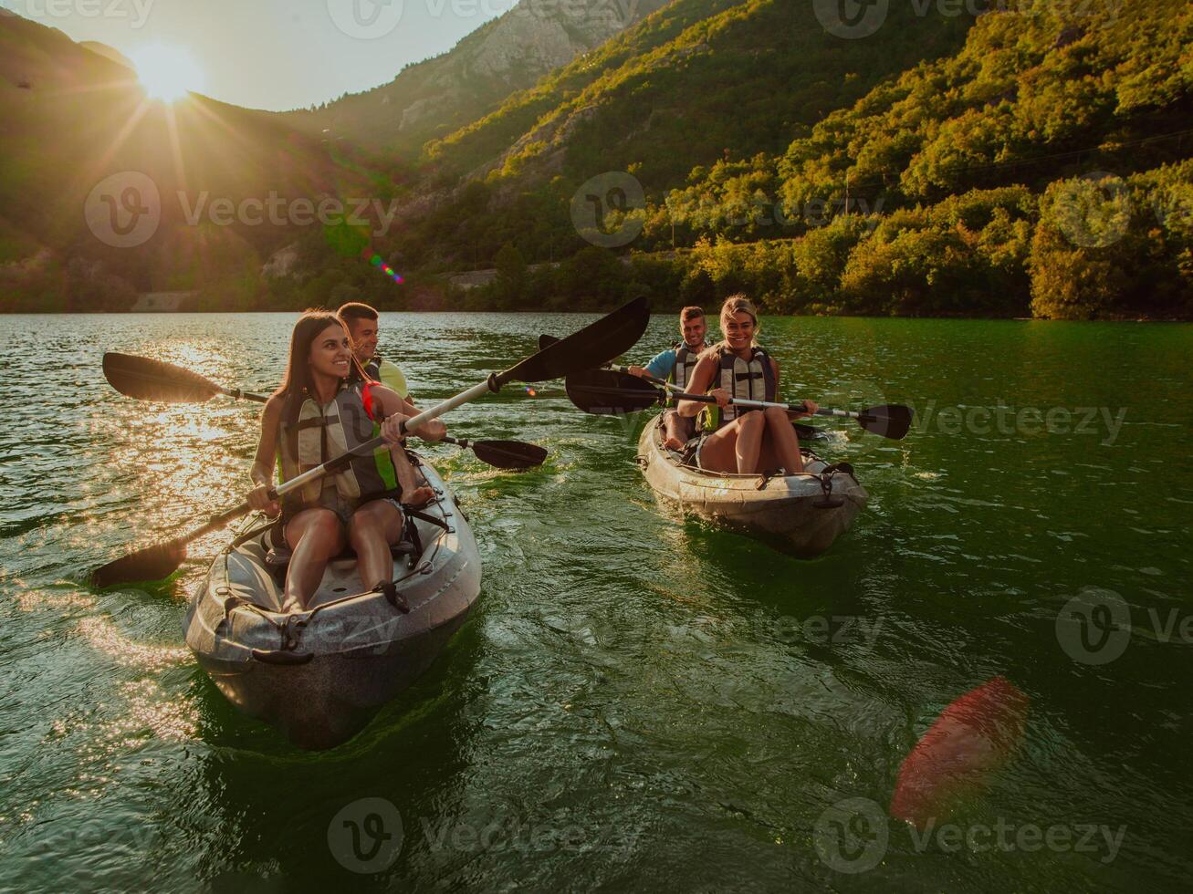 A group of friends enjoying fun and kayaking exploring the calm river, surrounding forest and large natural river canyons during an idyllic sunset. photo