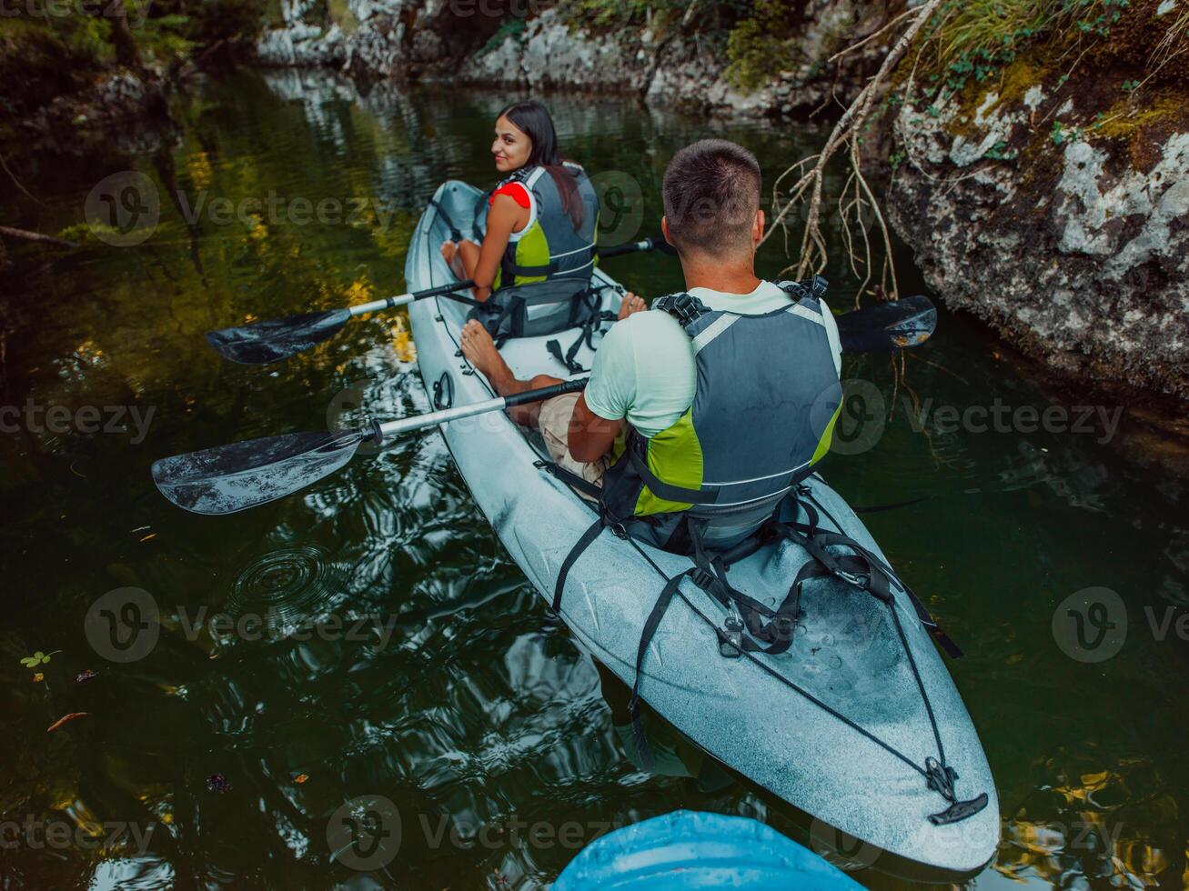 A young couple enjoying an idyllic kayak ride in the middle of a beautiful river surrounded by forest greenery photo