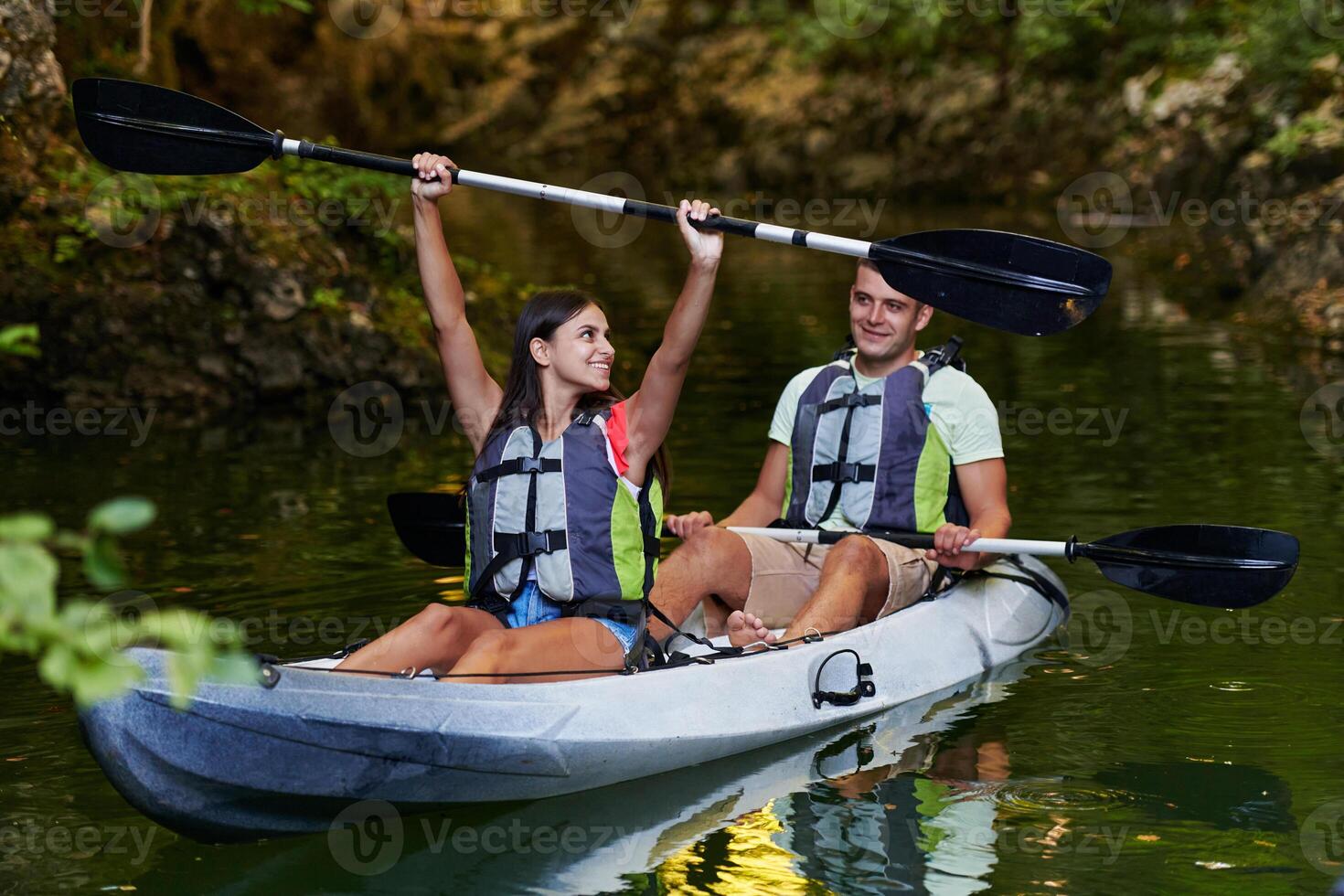 A young couple enjoying an idyllic kayak ride in the middle of a beautiful river surrounded by forest greenery photo