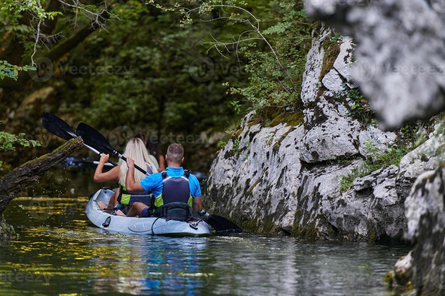 A young couple enjoying an idyllic kayak ride in the middle of a beautiful river surrounded by forest greenery photo
