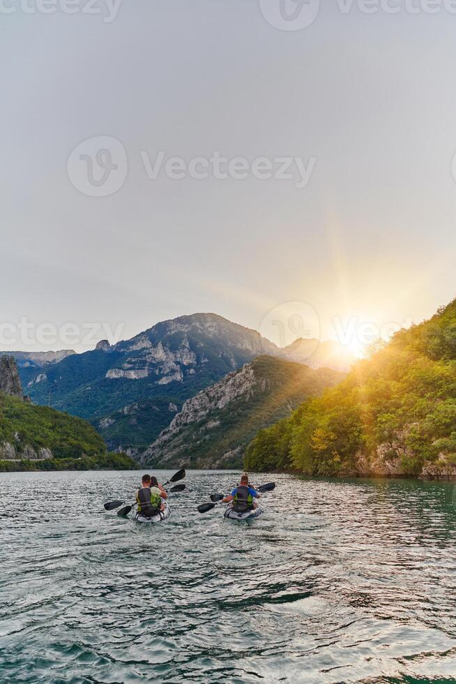 A group of friends enjoying fun and kayaking exploring the calm river, surrounding forest and large natural river canyons during an idyllic sunset. photo