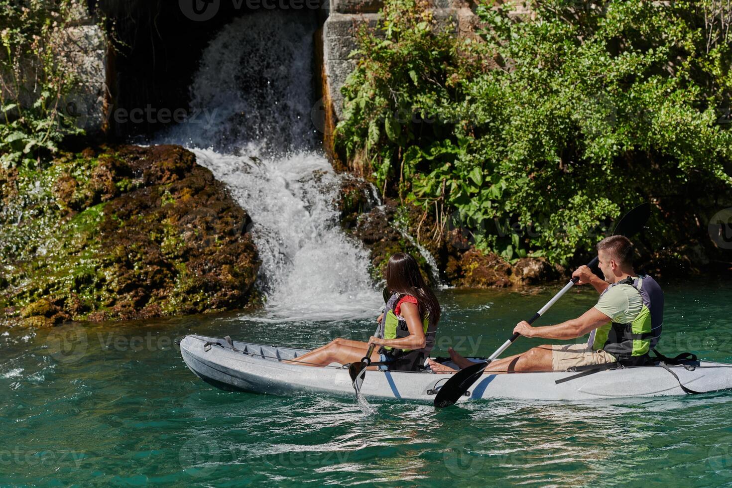 A young couple enjoying an idyllic kayak ride in the middle of a beautiful river surrounded by forest greenery photo