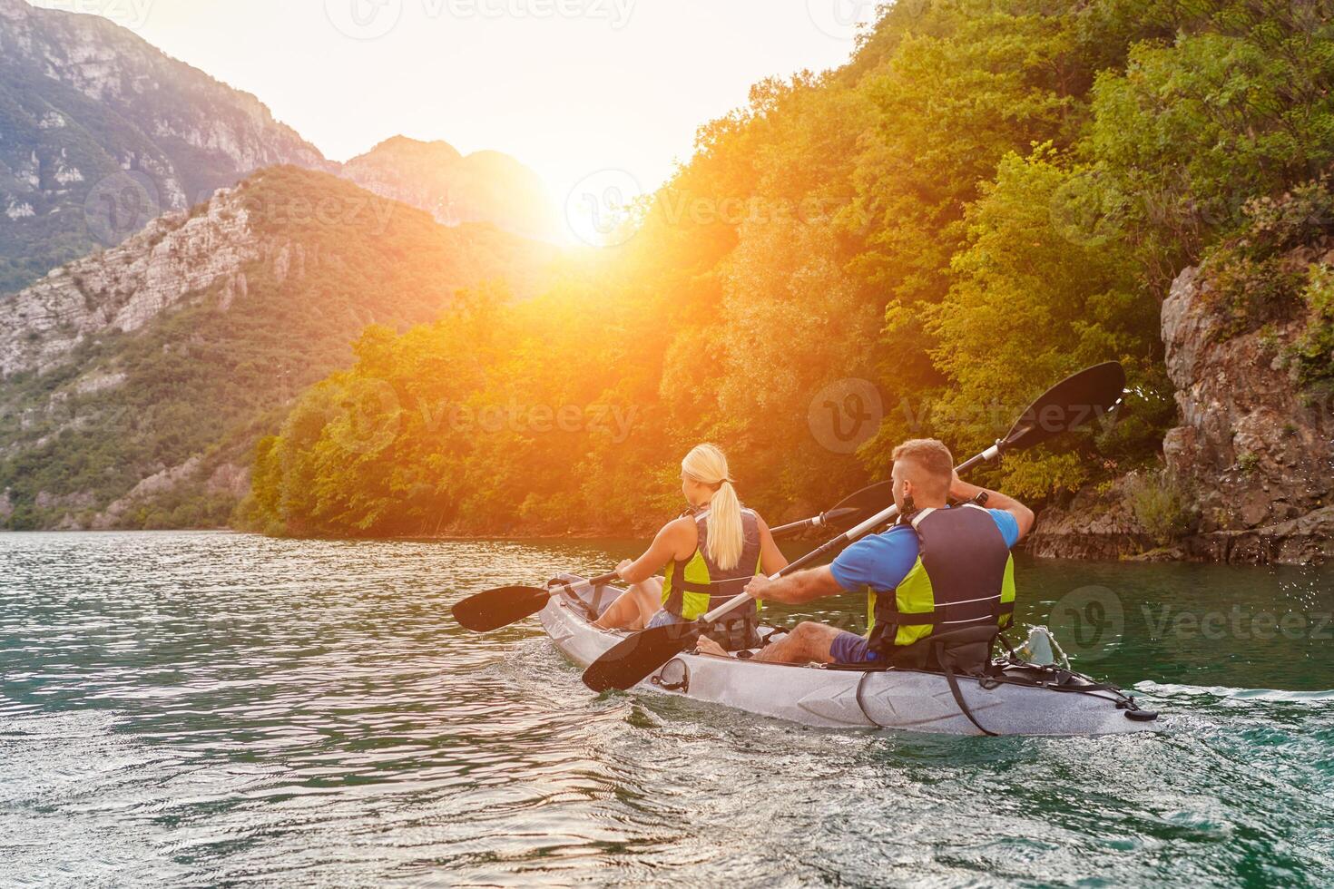 A group of friends enjoying fun and kayaking exploring the calm river, surrounding forest and large natural river canyons during an idyllic sunset. photo