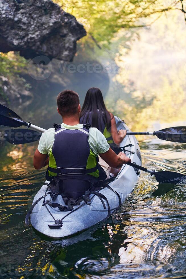 A young couple enjoying an idyllic kayak ride in the middle of a beautiful river surrounded by forest greenery photo