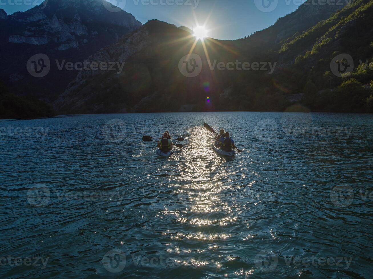 A group of friends enjoying fun and kayaking exploring the calm river, surrounding forest and large natural river canyons during an idyllic sunset. photo