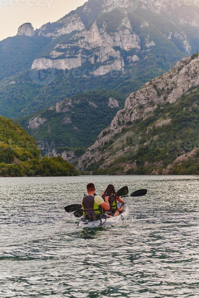 A young couple enjoying an idyllic kayak ride in the middle of a beautiful river surrounded by forest greenery in sunset time photo