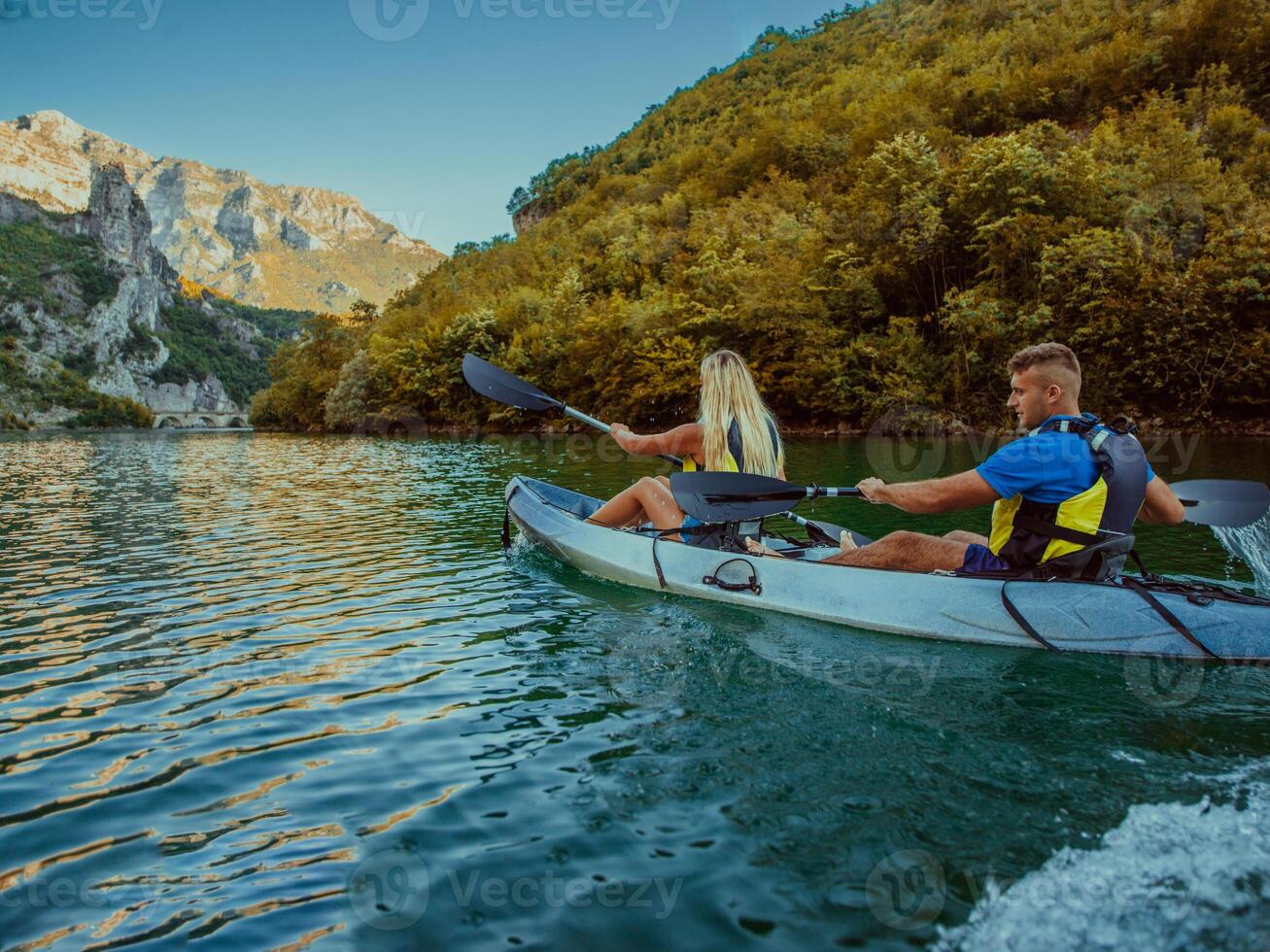 A young couple enjoying an idyllic kayak ride in the middle of a beautiful river surrounded by forest greenery photo