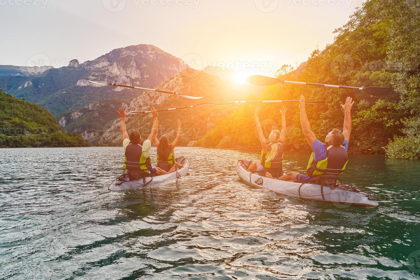 A group of friends enjoying fun and kayaking exploring the calm river, surrounding forest and large natural river canyons during an idyllic sunset. photo