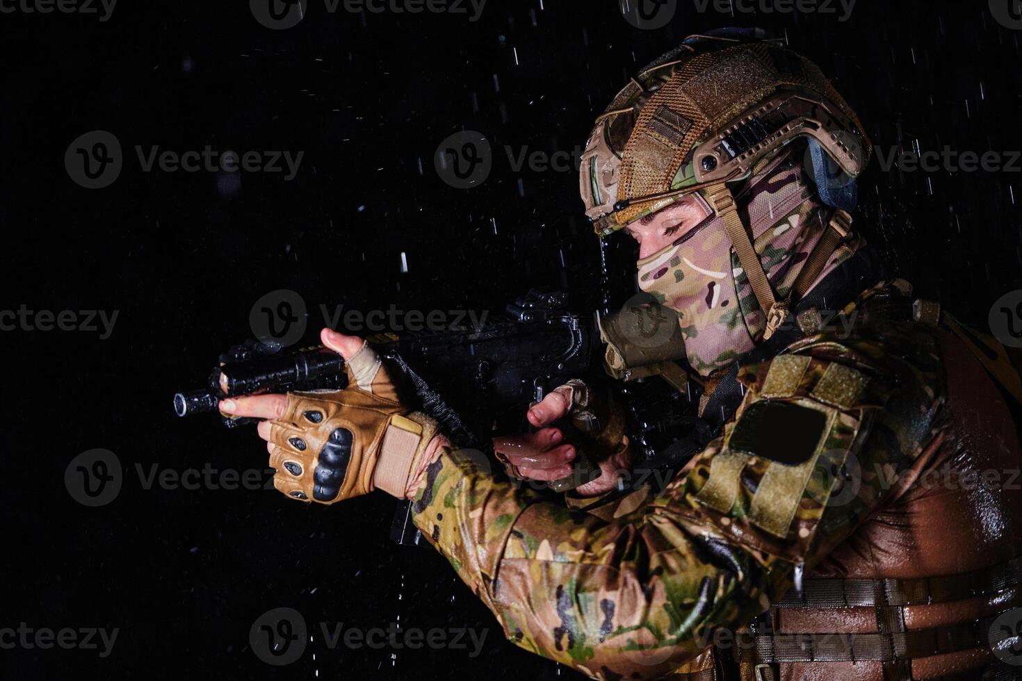 Army soldier in Combat Uniforms with an assault rifle, plate carrier and combat helmet going on a dangerous mission on a rainy night. photo