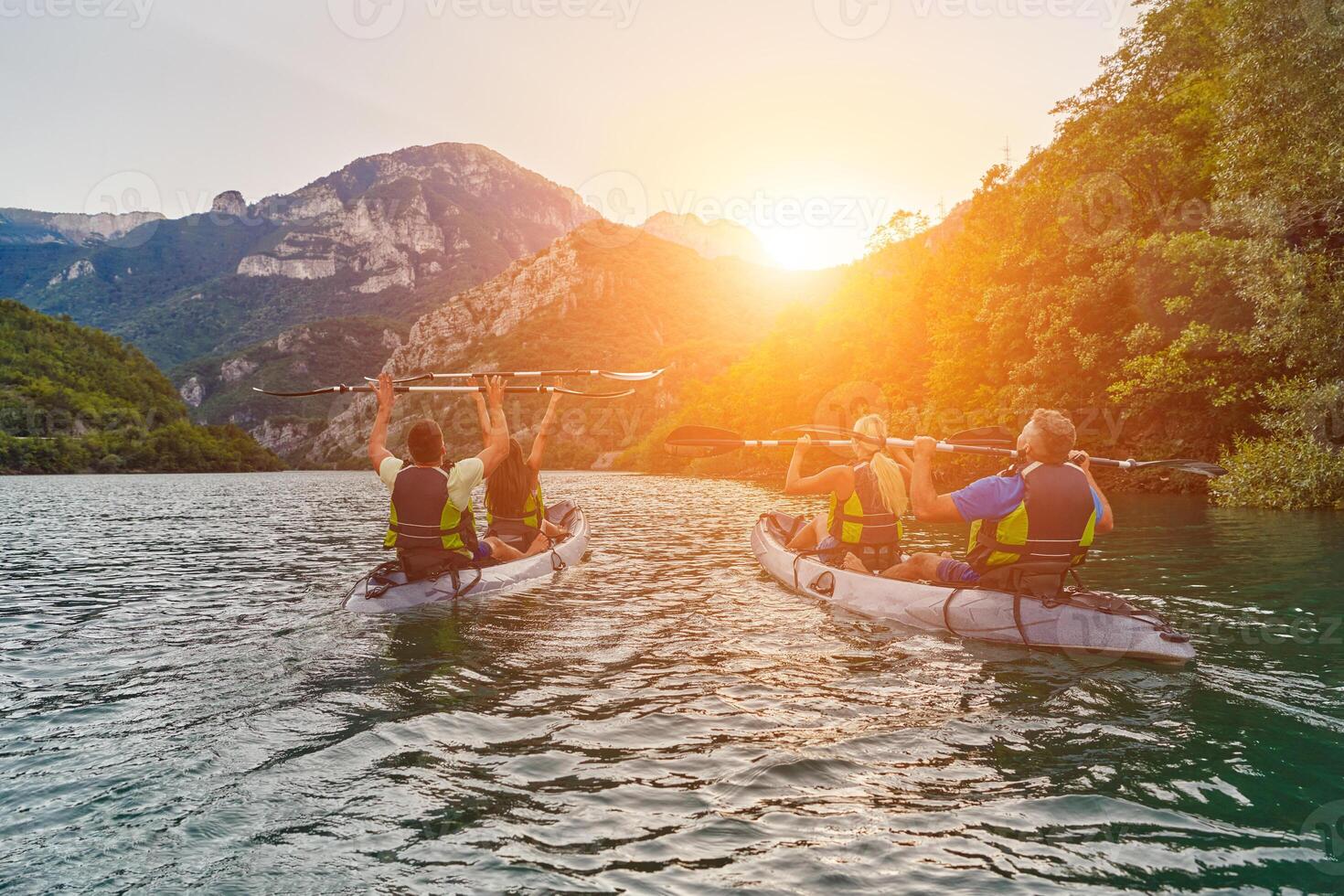 A group of friends enjoying fun and kayaking exploring the calm river, surrounding forest and large natural river canyons during an idyllic sunset. photo