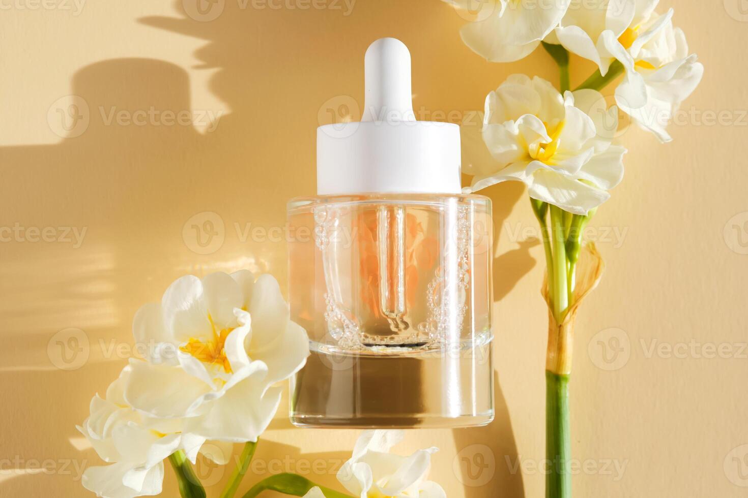 A bottle of luxury serum with petals on a beige background with daffodils. photo