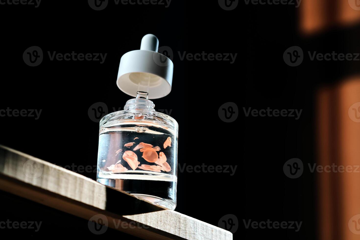 Serum bottle with petals on a dark background. photo
