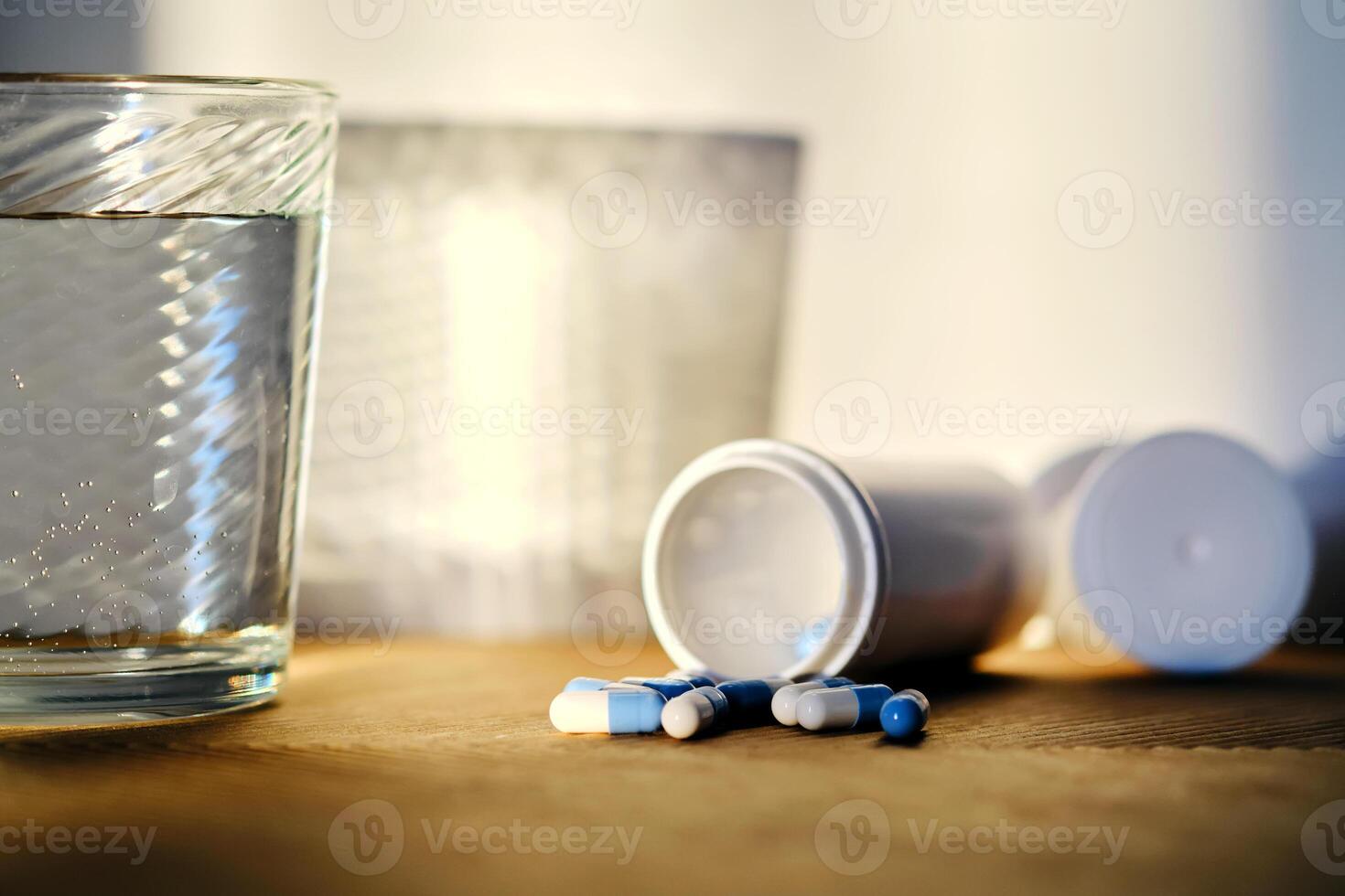 A glass of water and a bottle of pills in the sunlight. photo