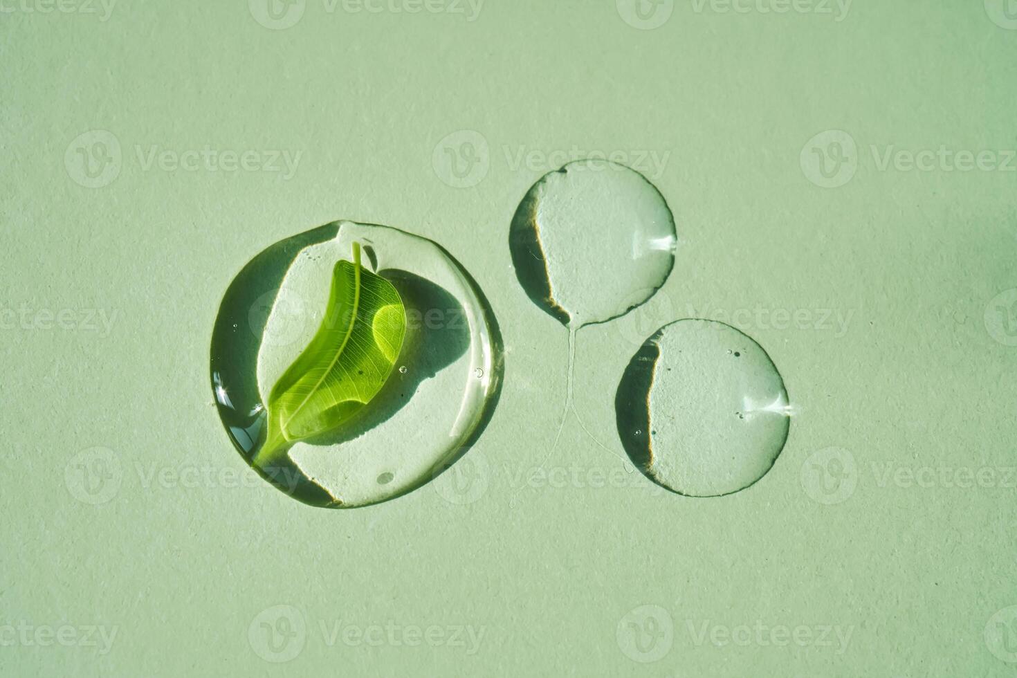 Drop of face serum with green leaf on green background. photo