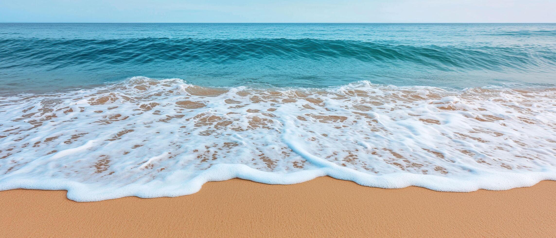 Ocean wave reaching sandy beach shoreline with white sea foam washing over the golden sand. The blue water contrasts with the warm tones of the beach under a clear sky. photo