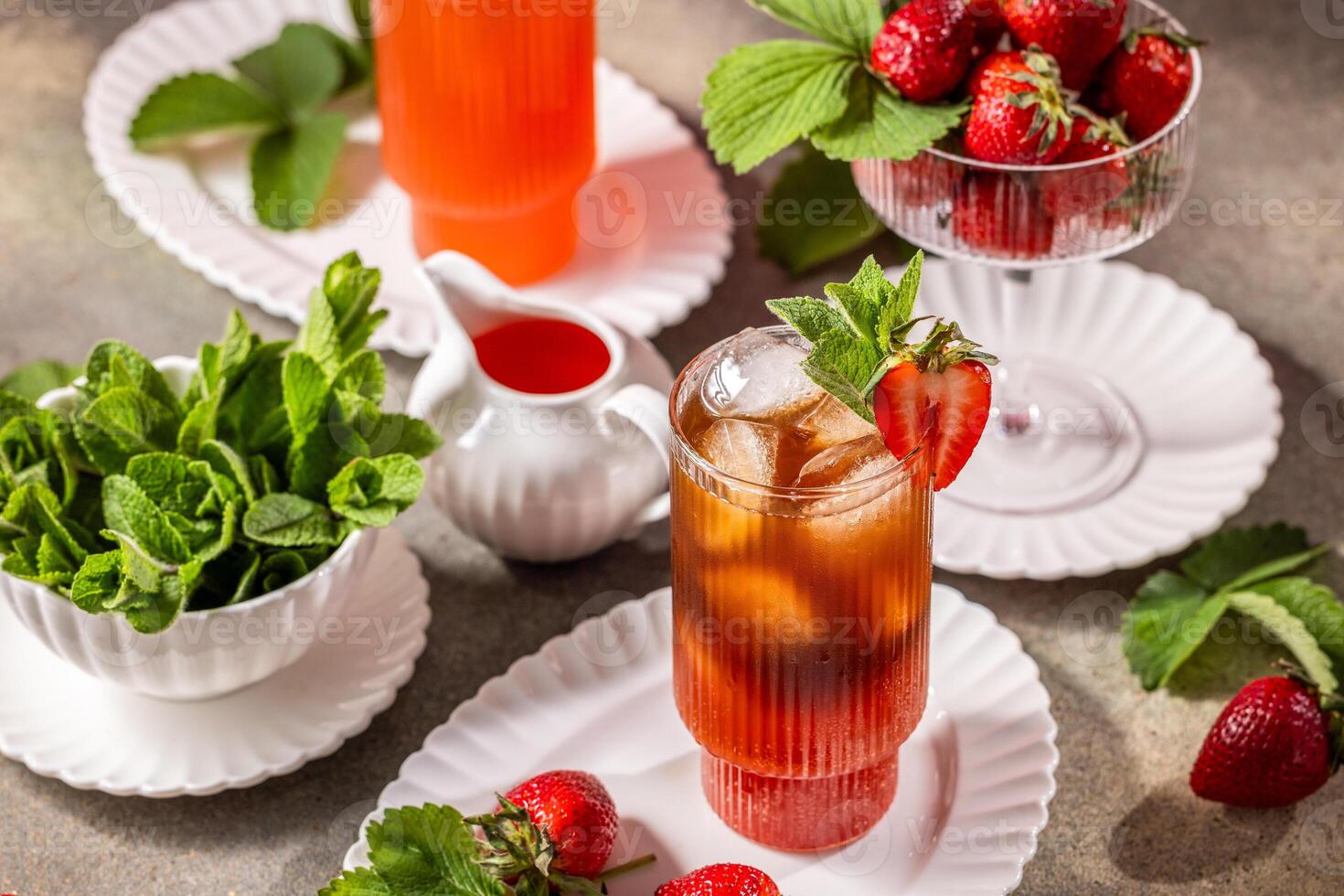 Glass of strawberry iced tea decorated with fresh mint and strawberries, accompanied by ingredients on a table photo