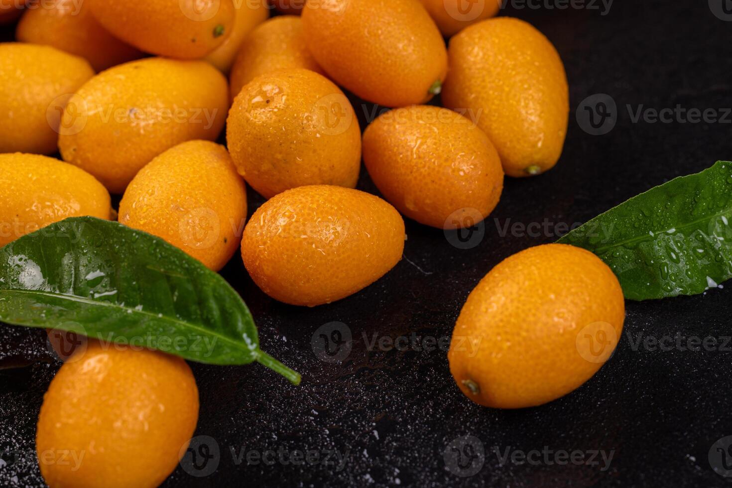 Fresh kumquats with leaves resting on dark surface photo