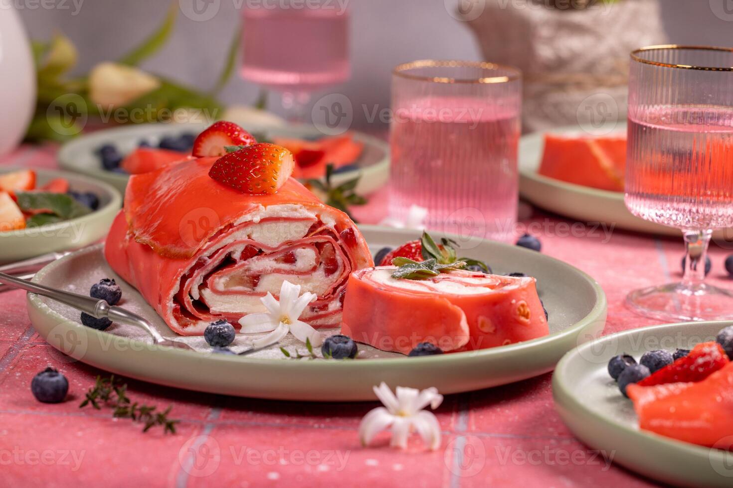 Delicious pink strawberry cake roll decorated with fresh berries and flowers on table setting photo