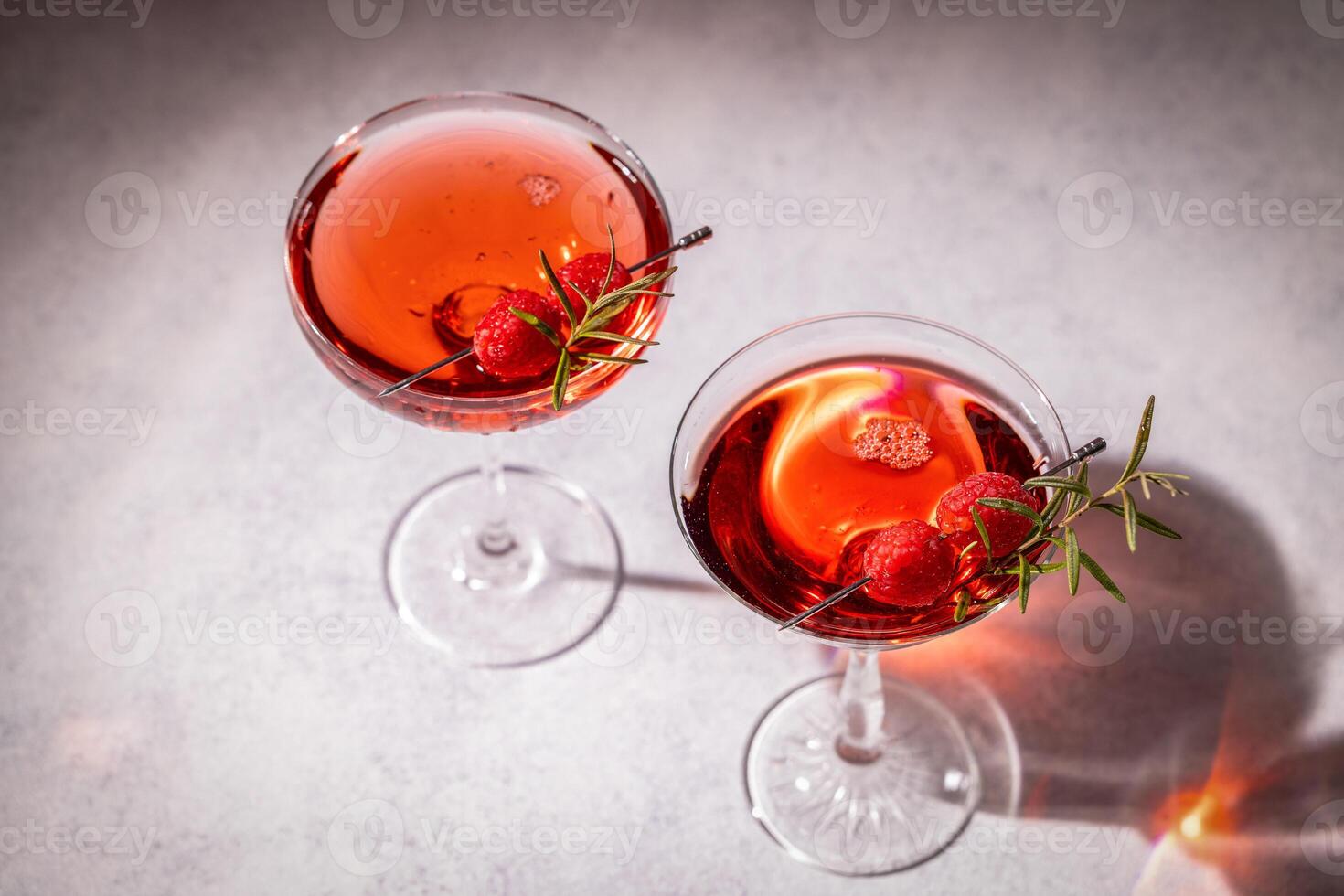 Two elegant cocktails garnished with raspberries and rosemary on grey table photo