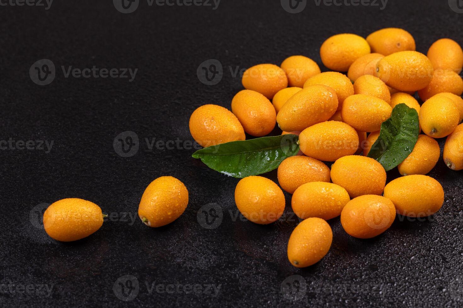 Fresh kumquats with leaves resting on wet black surface photo