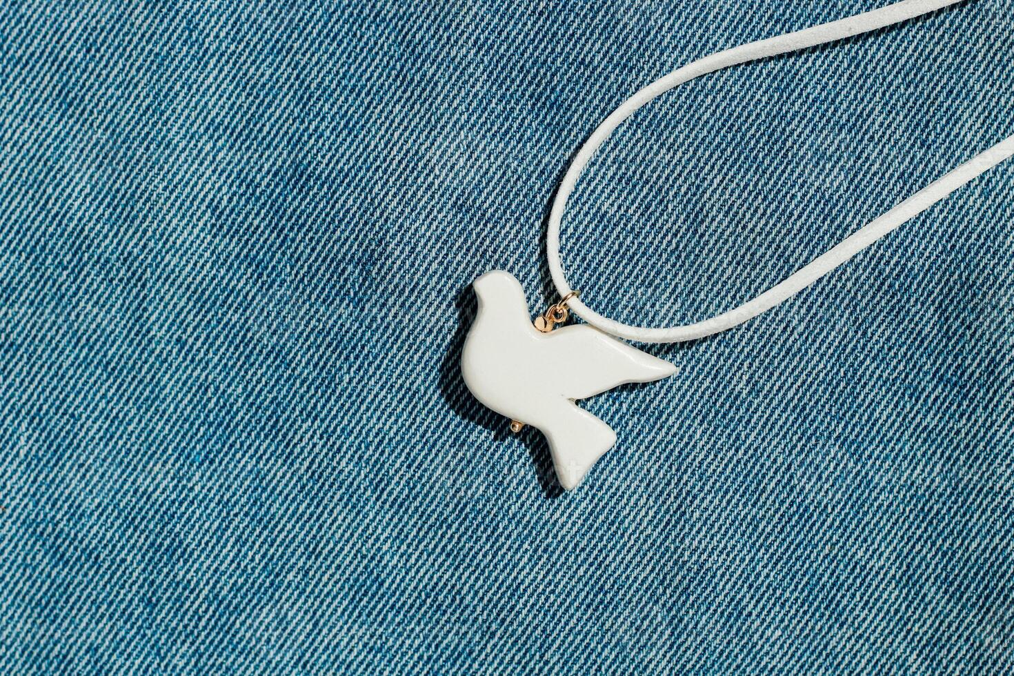 bijouterie white bird of polymer clay on the background of denim fabric photo