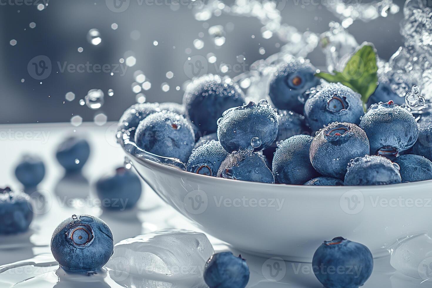 A white bowl filled with ripe blueberries and ice sits on a white table, with water droplets scattered around. photo
