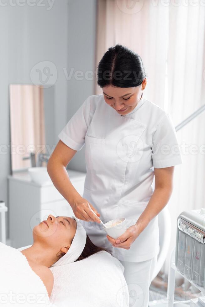 Dermatologist preparing face mask for client in beauty spa photo