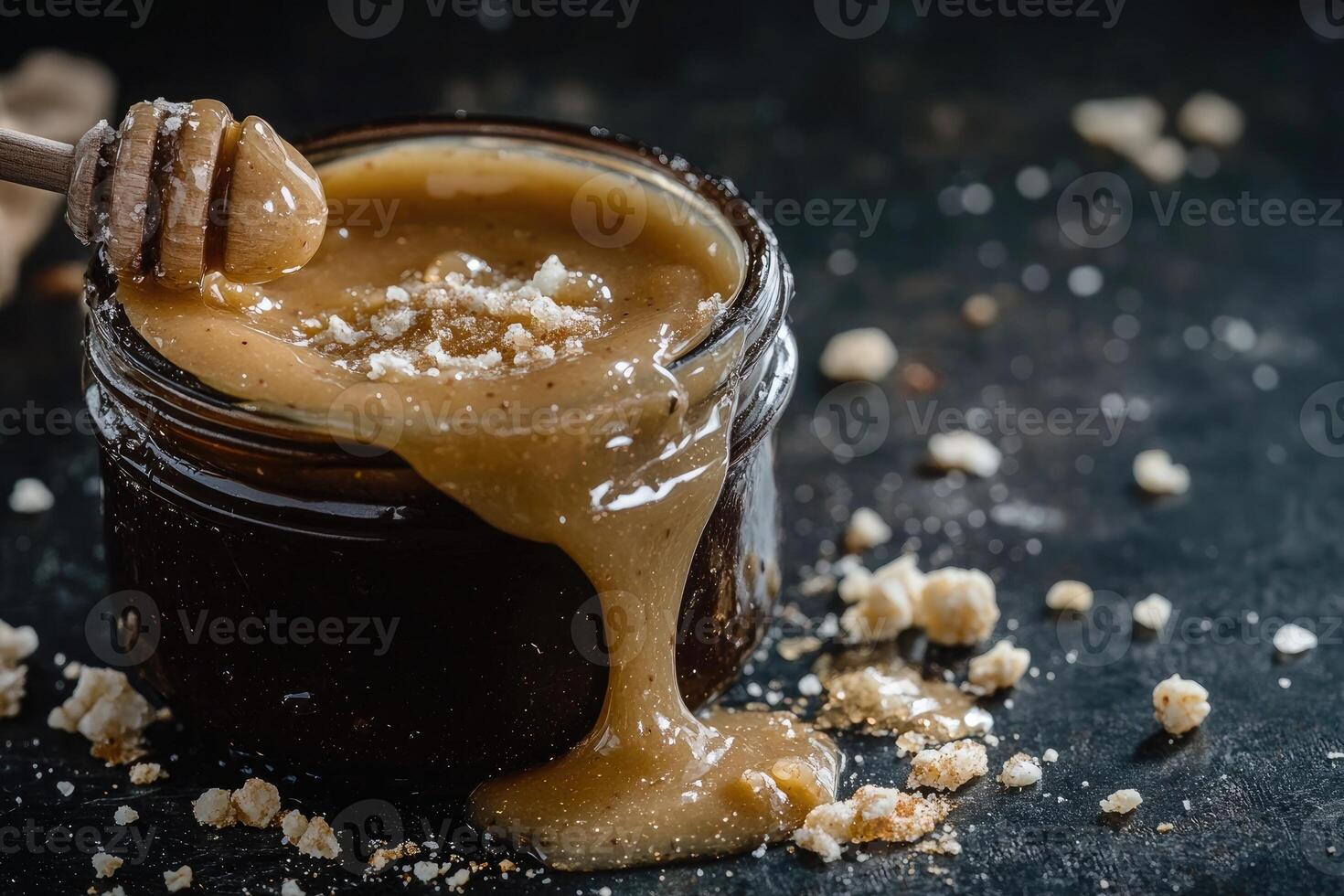 Indulgent mixture of tahini and honey spilling from a jar with sea salt flakes on a dark, rustic surface photo