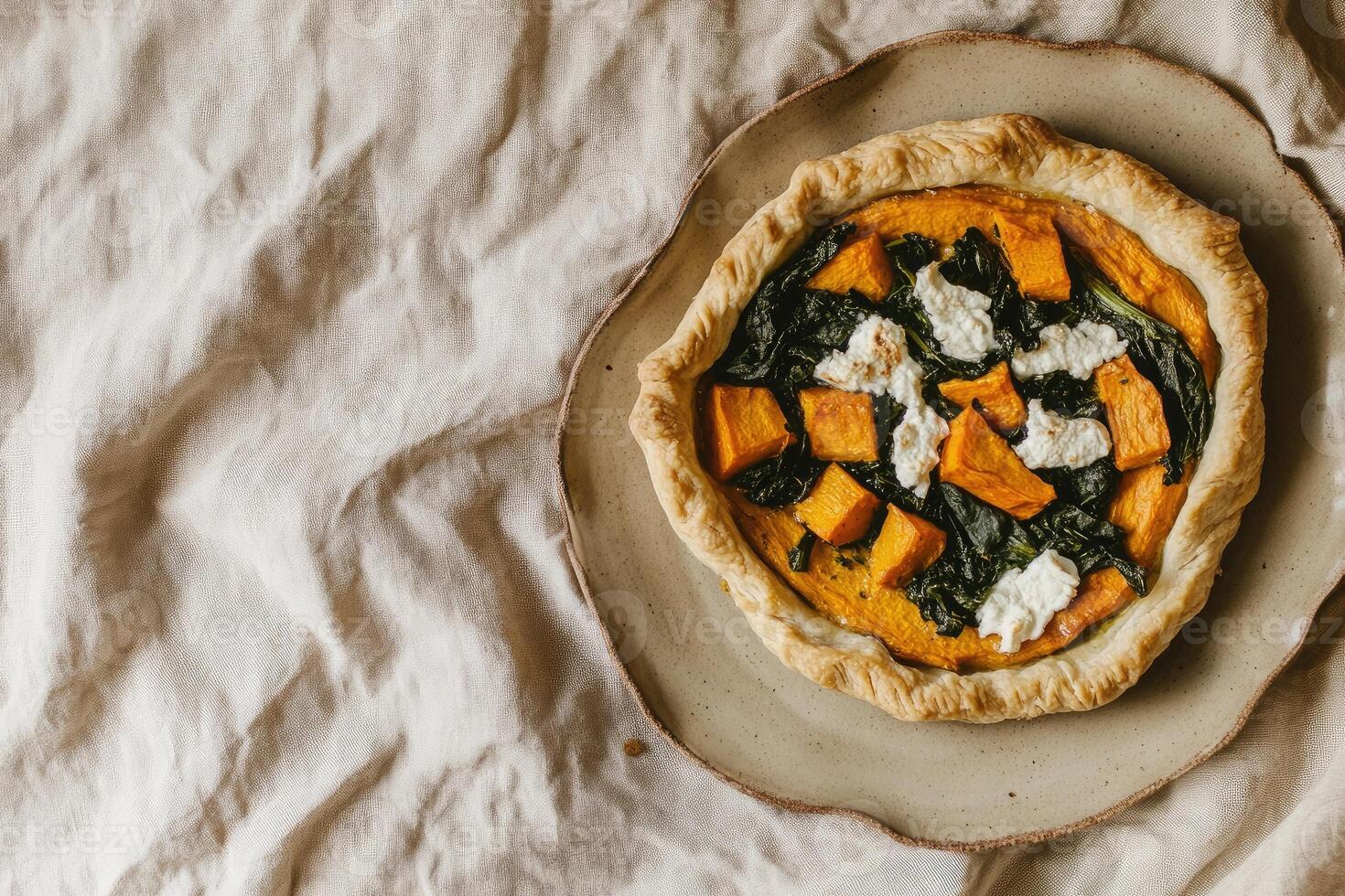 Vegetarian open pie with sweet potatoes, spinach, and goat cheese served on handmade ceramic plate in natural light photo