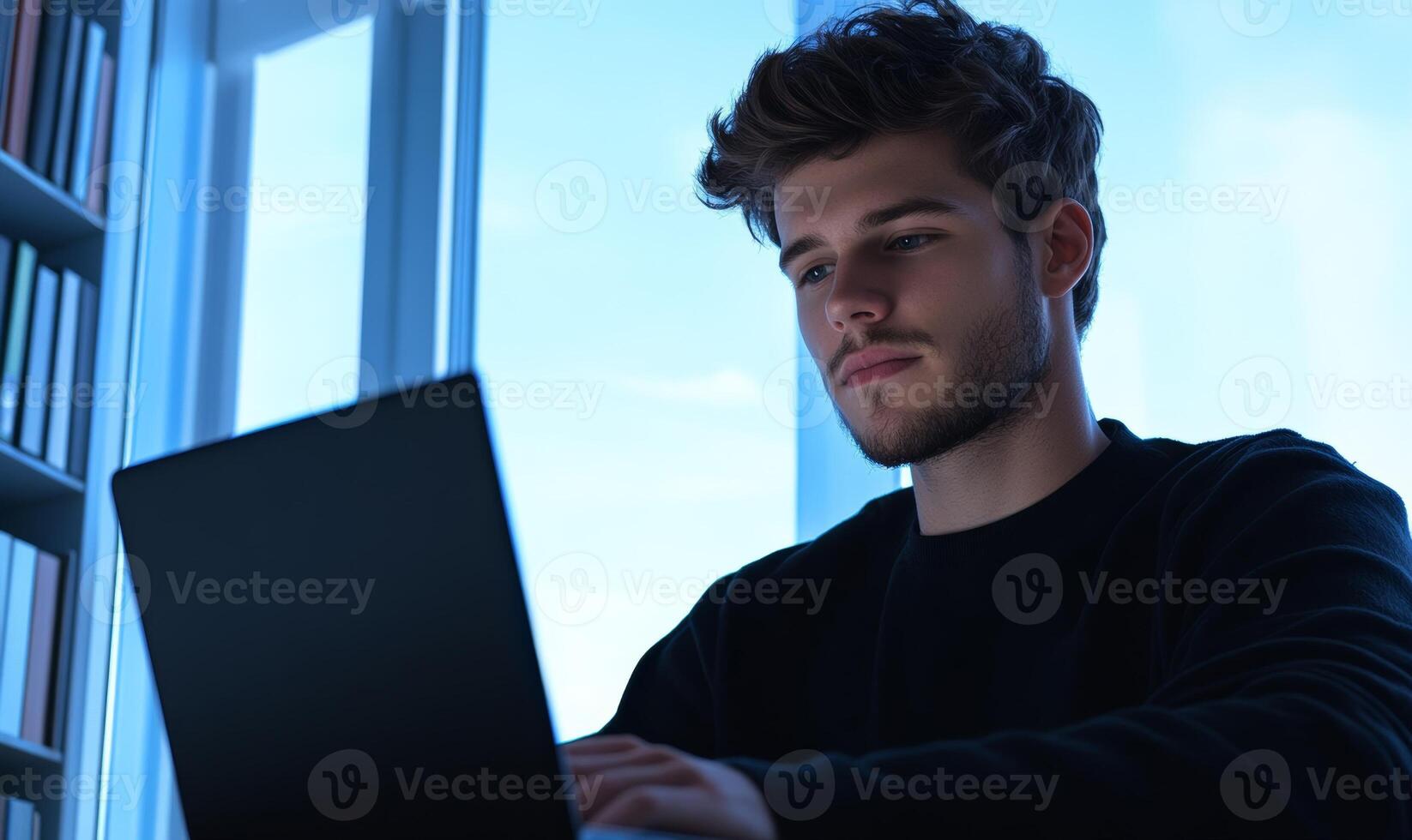 student typing on a laptop in a library, surrounded by books and natural light from large windows photo