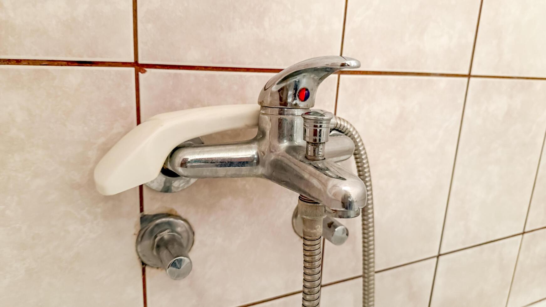 Close up of a modern bathroom faucet with a handheld showerhead on tiled wall, highlighting home maintenance and plumbing solutions photo