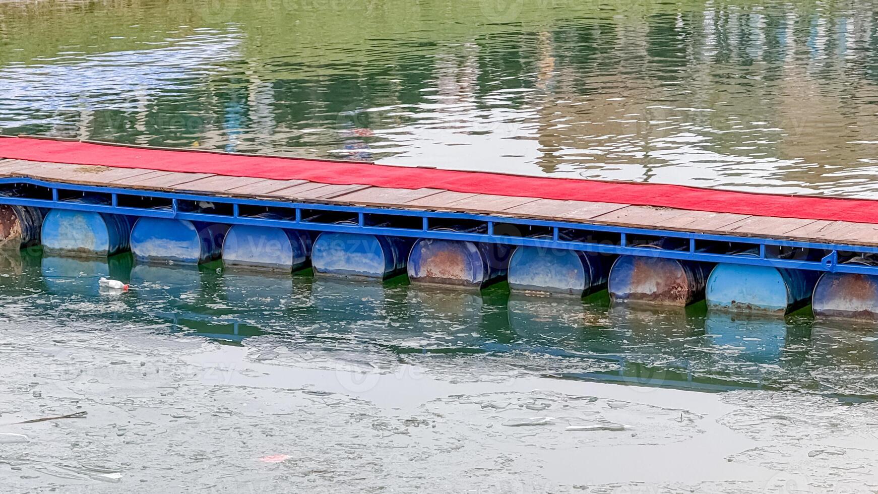 A floating bridge with a red surface rests on a tranquil body of water, symbolizing innovative transportation solutions photo