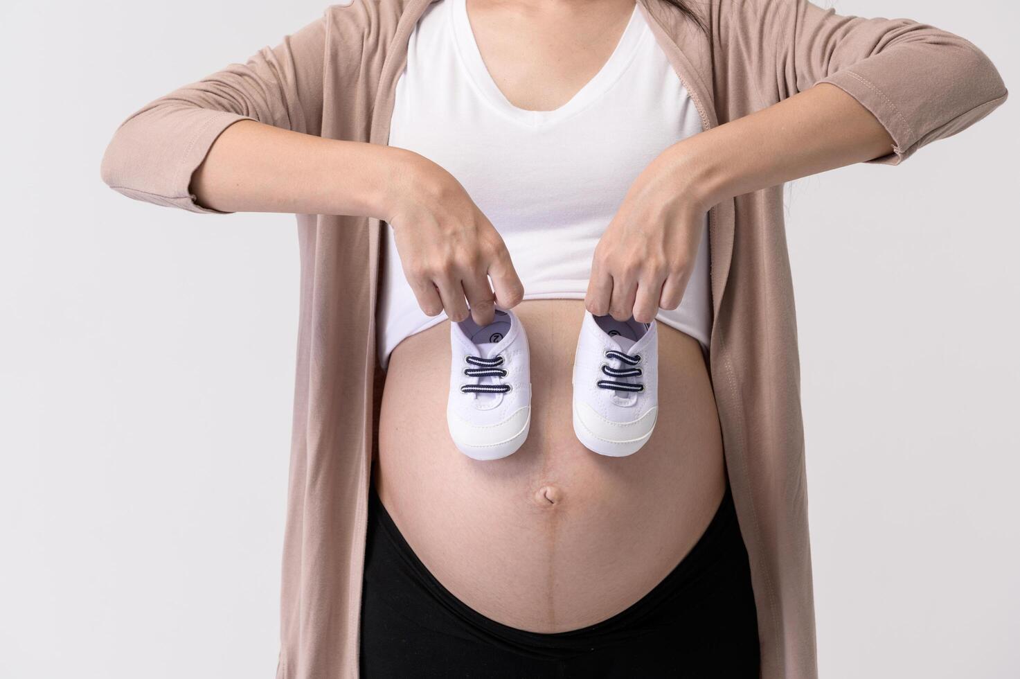 A Portrait of Beautiful pregnant woman holding baby shoes over white background studio photo