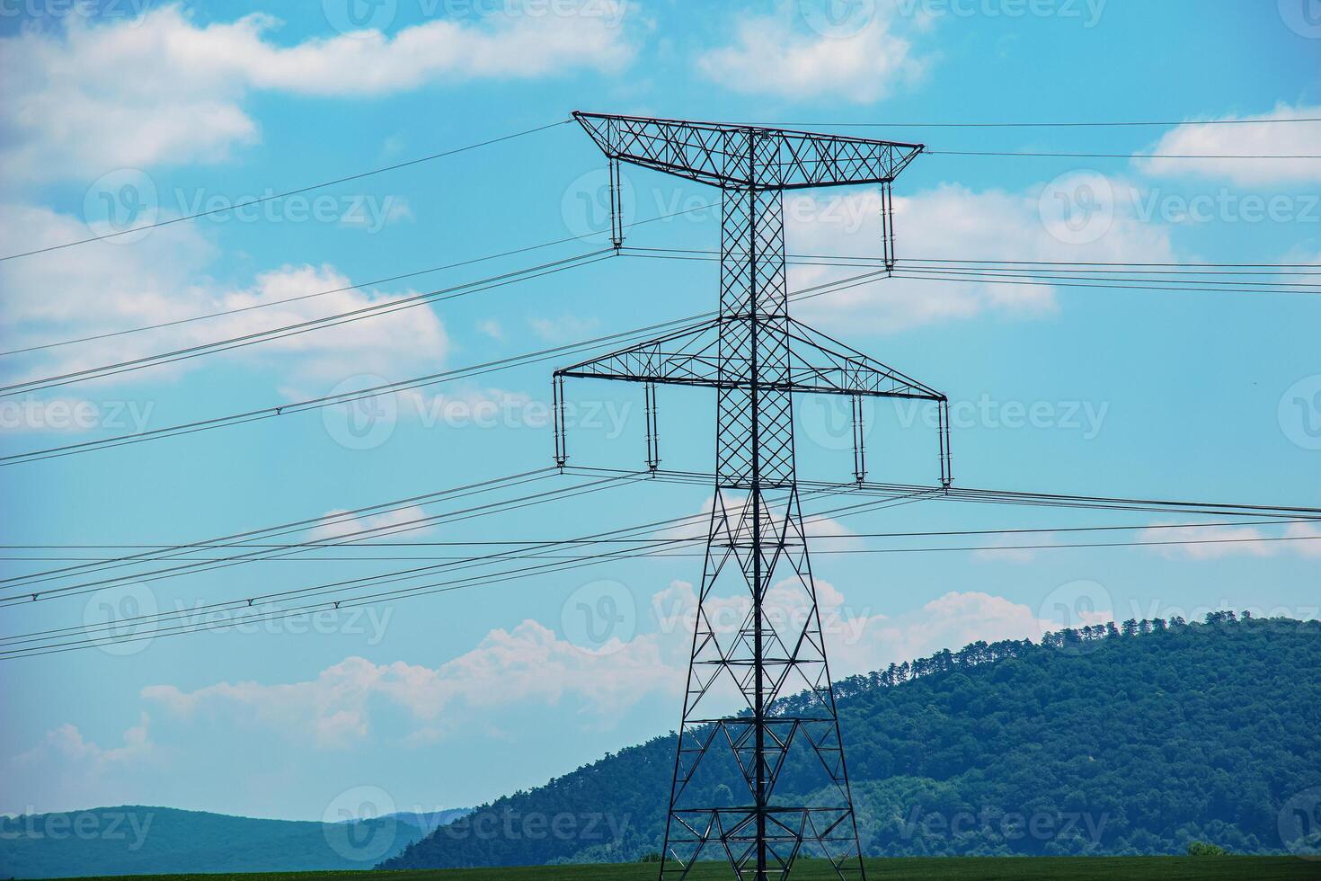 High voltage lines power pylons in a green landscape on a sunny day with clouds in the blue sky. photo