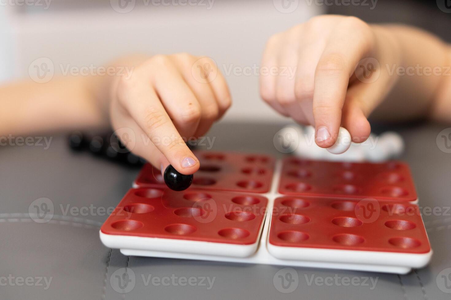 Childrens hands place marbles on the game board, enjoying a moment of fun and challenge with friends. The game is a joyful. Kids enjoy a game on the board with black and white marbles. photo