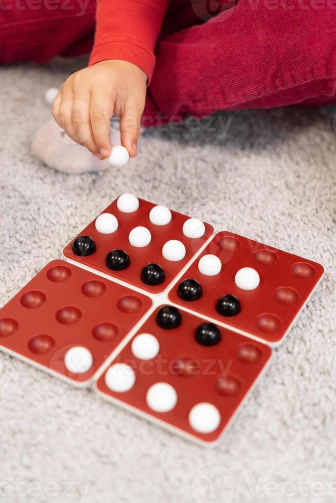 One hand hovers over the game board, holding black and white marbles. Child is ready to place the marbles, carefully thinking about the next move. photo