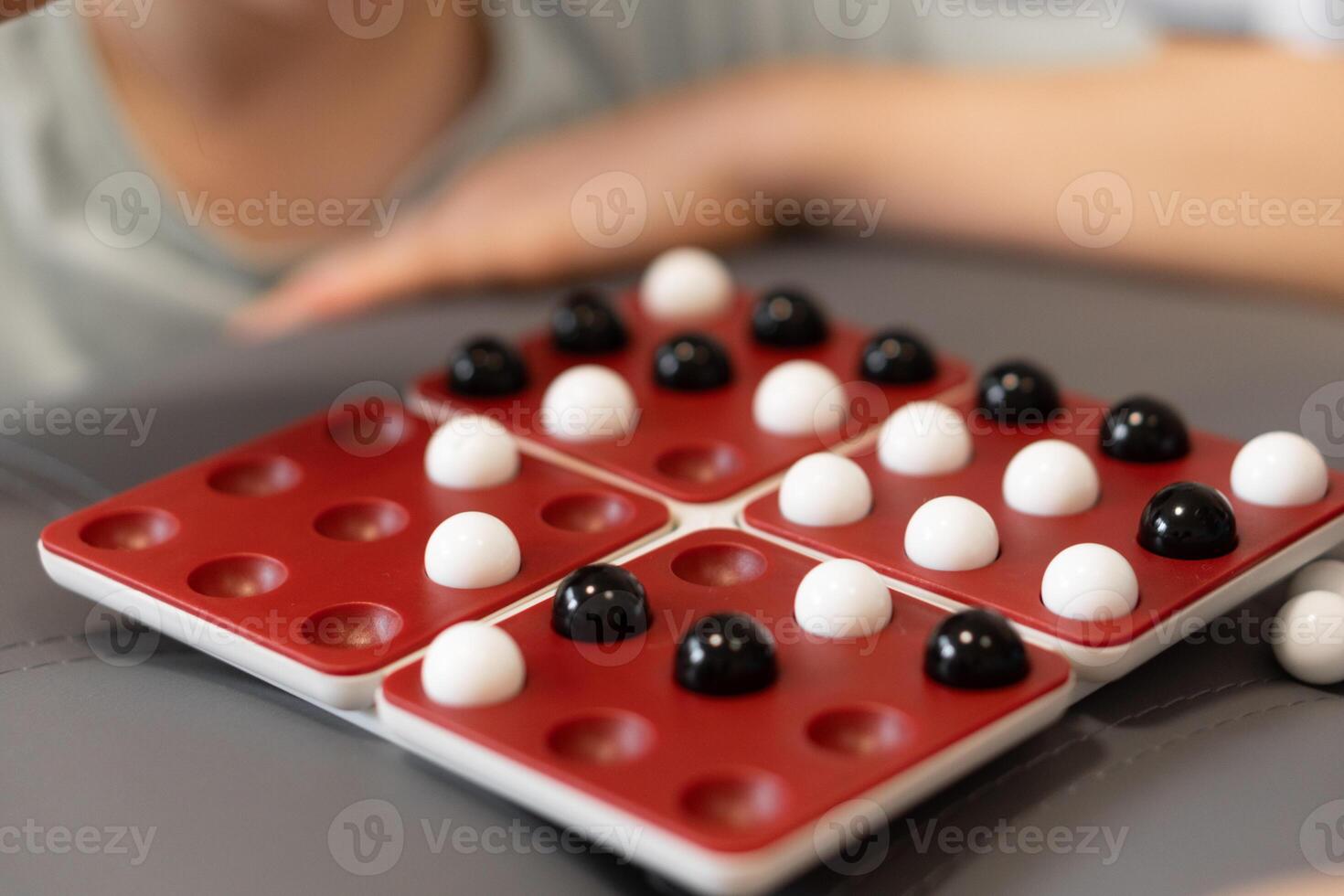 Kids place black and white marbles on the board, carefully planning each move. The game offers them a chance to learn strategy while having fun together. photo