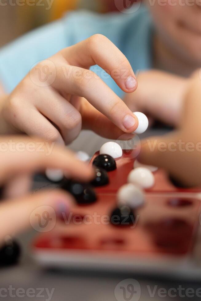 Children gather around the table to play, placing marbles on the game board. Laughter and strategy go hand in hand as they enjoy every move. photo