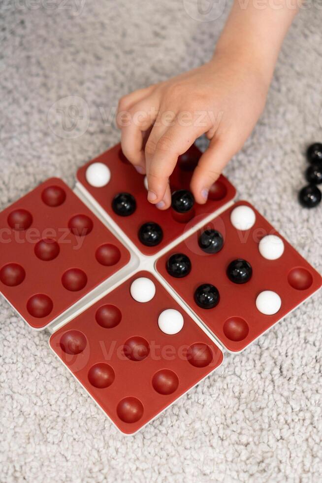 Children's hands move marbles on the game board, adjusting their strategy with each turn. The game is a fun test of skill and planning. photo