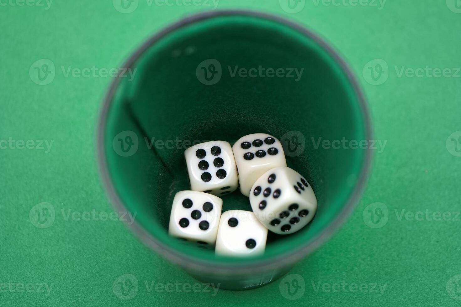 Various white dice with black dots resting inside a green cup se photo