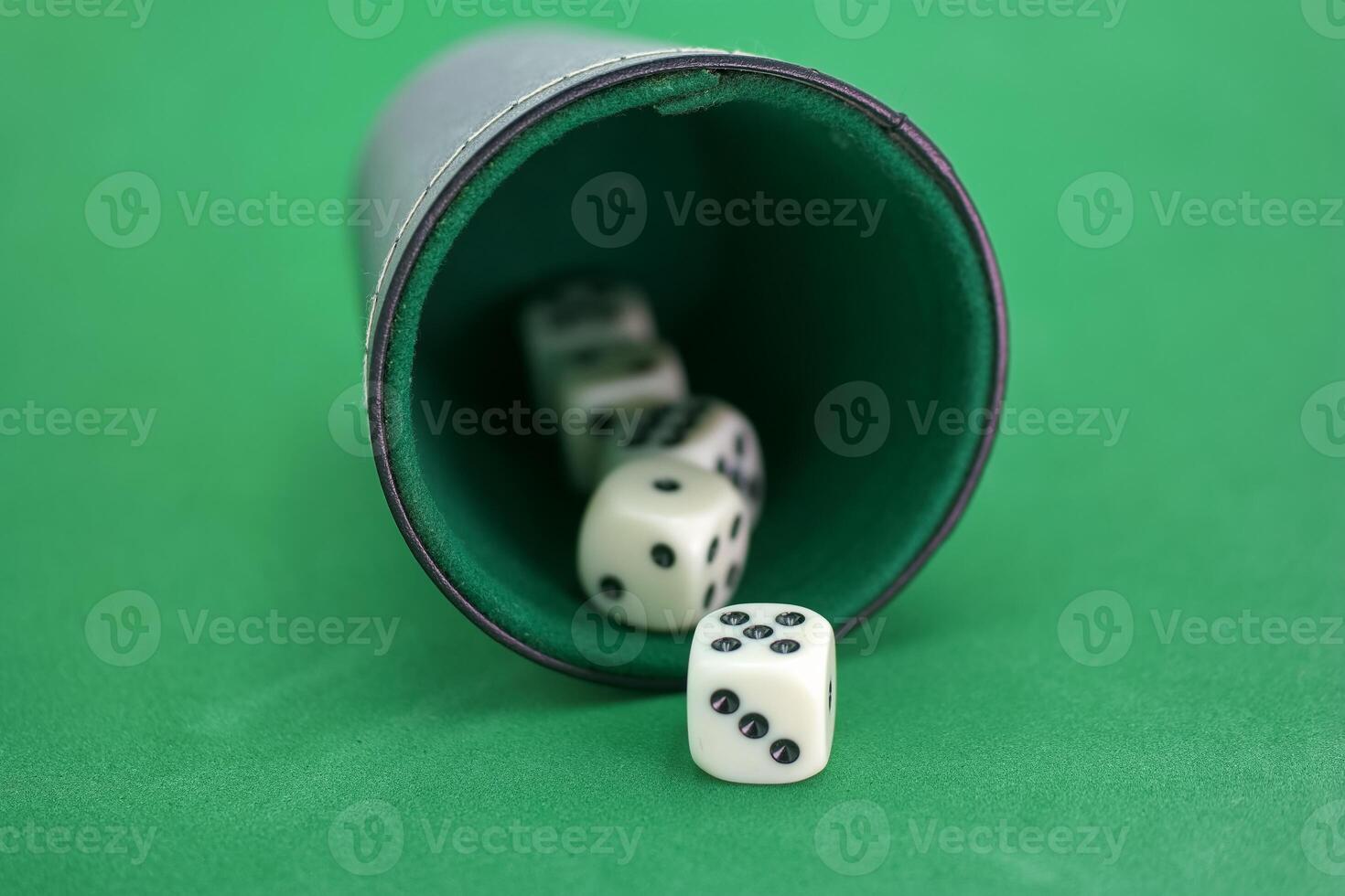 Rolling dice in a cup on a green photo