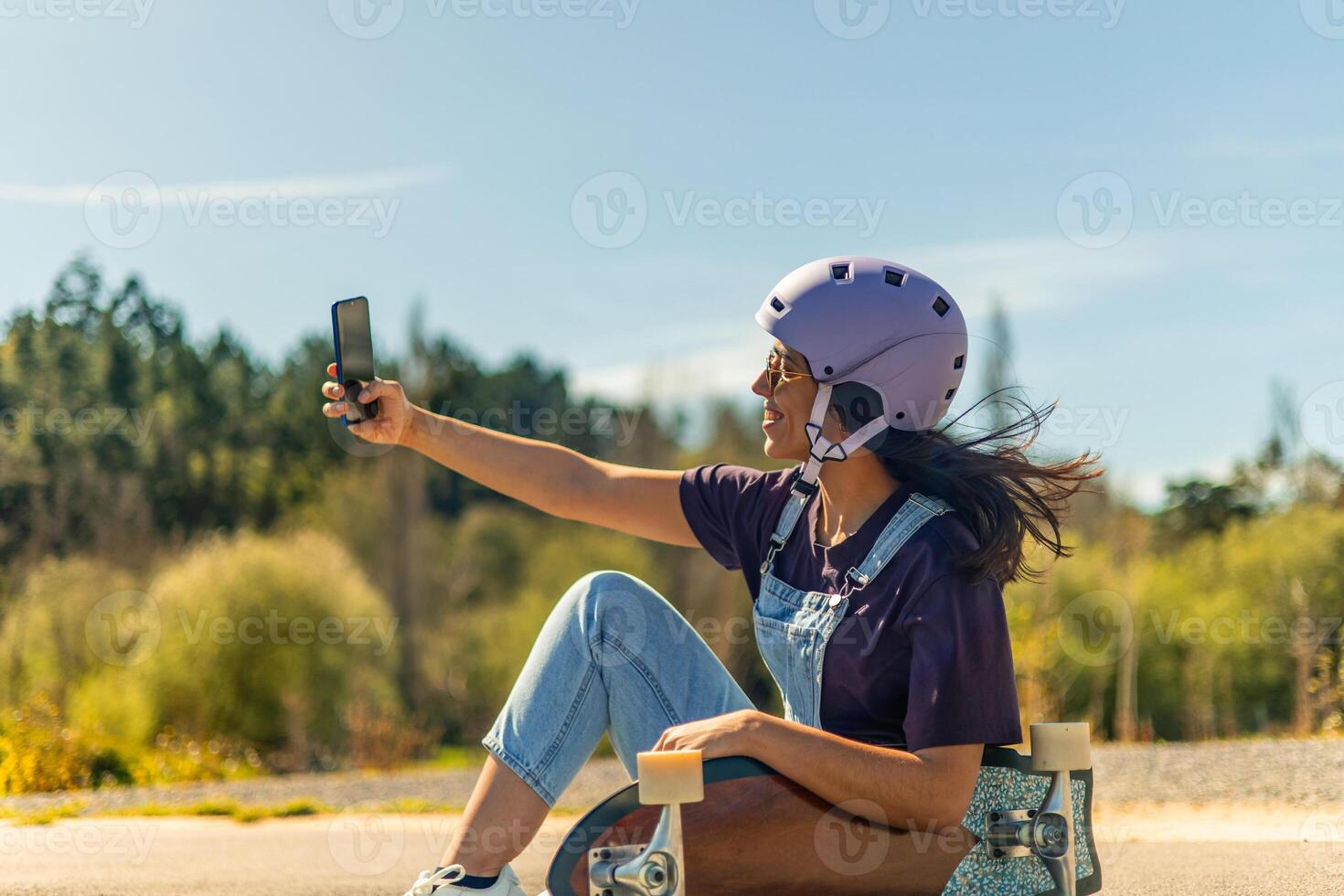 Latin skater taking a selfie with smartphone while sitting on her surfskate in pump track photo