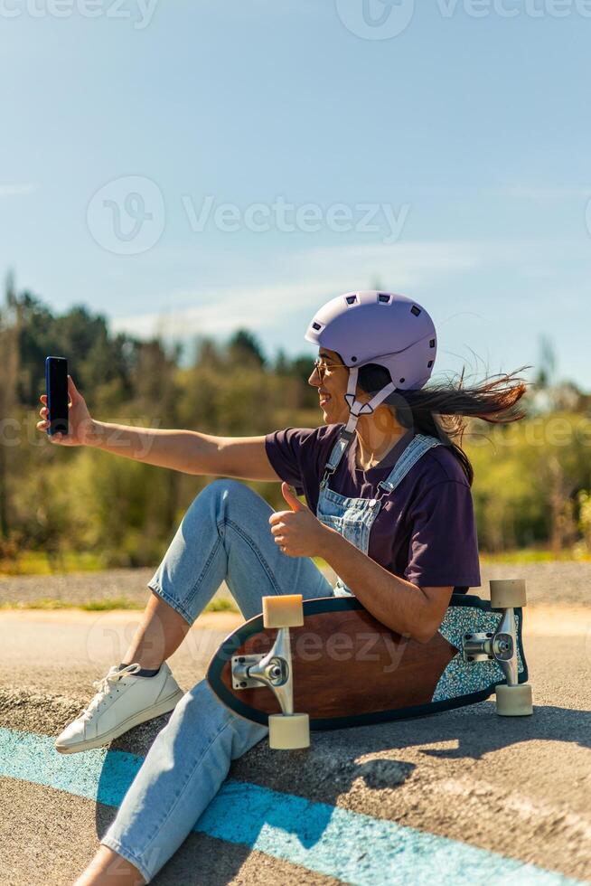 Latin skater taking selfie with smartphone and giving thumbs up in pump track photo
